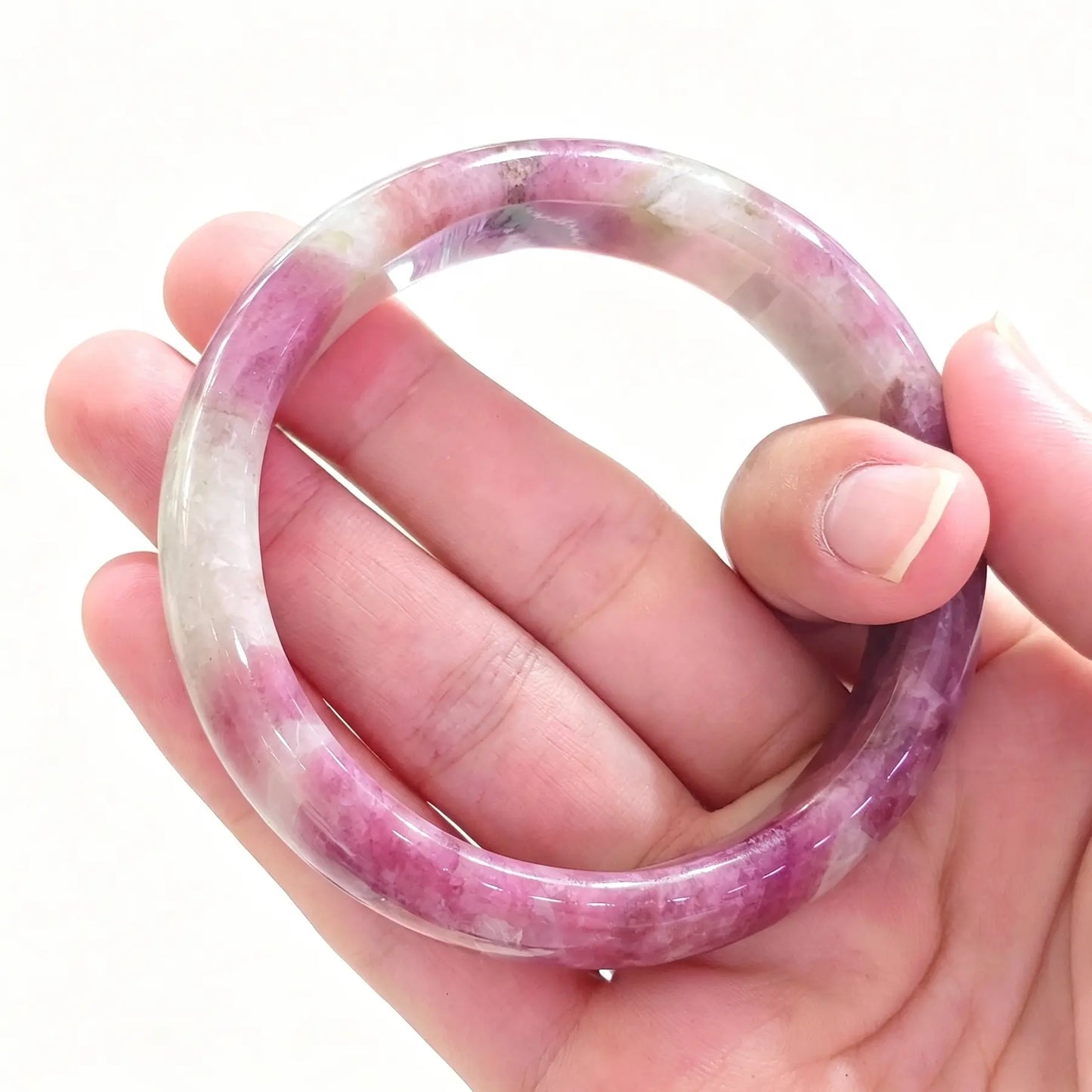 Hand holding a natural plum blossom tourmaline bangle displaying rich pink inclusions in translucent quartz