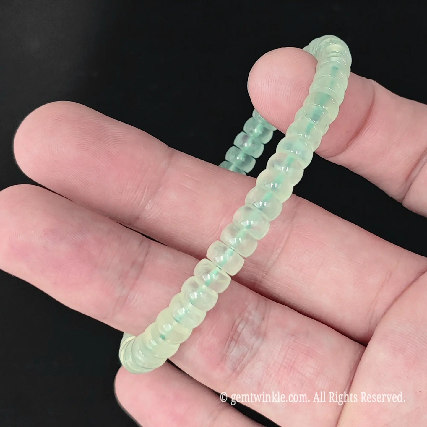 Natural prehnite small wheel bead bracelet held across fingers displaying smooth disc alignment
