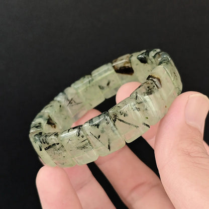 Natural prehnite with black tourmaline needles 16x11mm smooth block bracelet held close up showing translucent green matrix and black inclusions