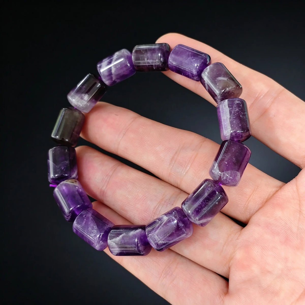 natural purple amethyst 14x10mm barrel bead bracelet held in hand against dark background