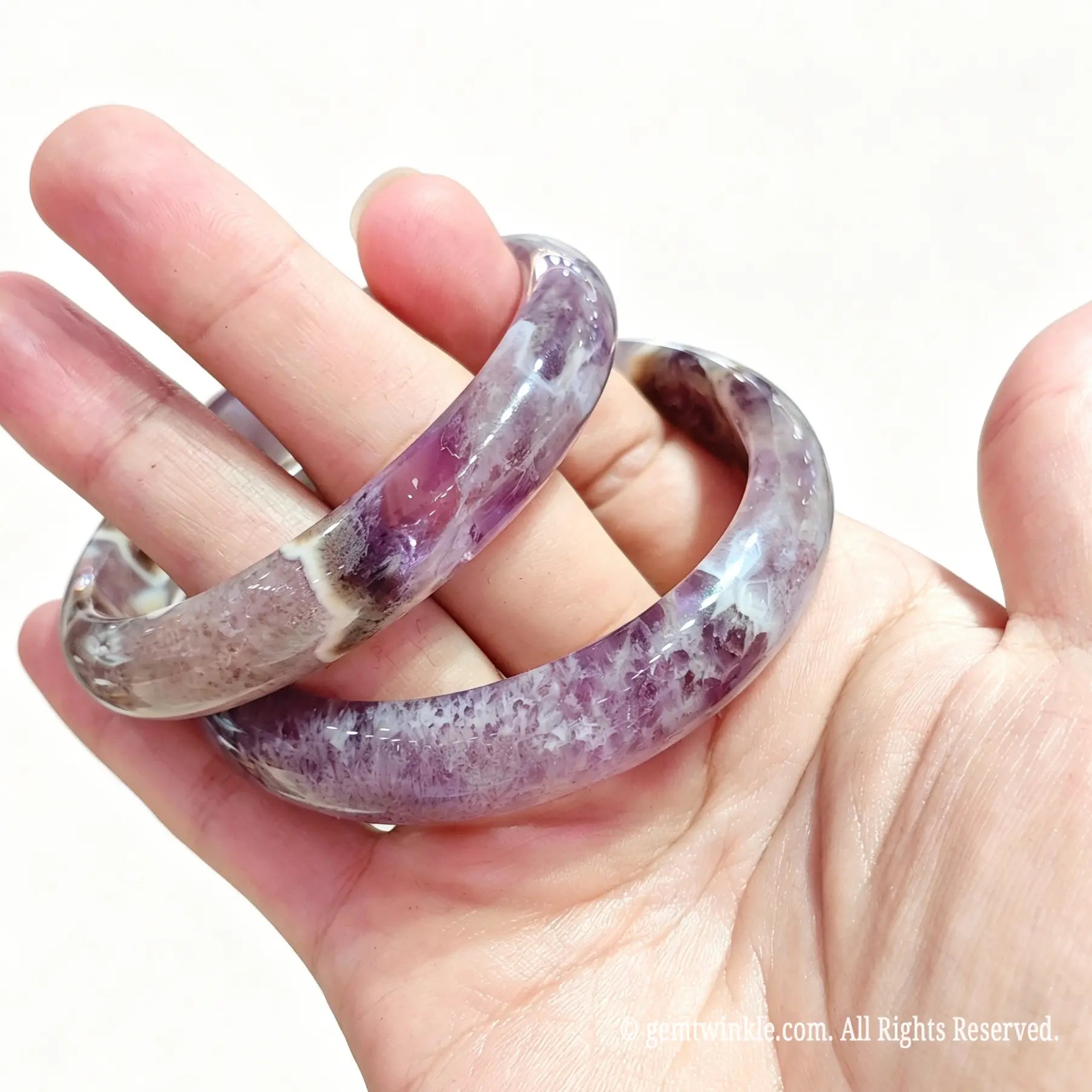 Pair of natural amethyst agate bangles held in hand showing smooth polish and translucent mineral layers