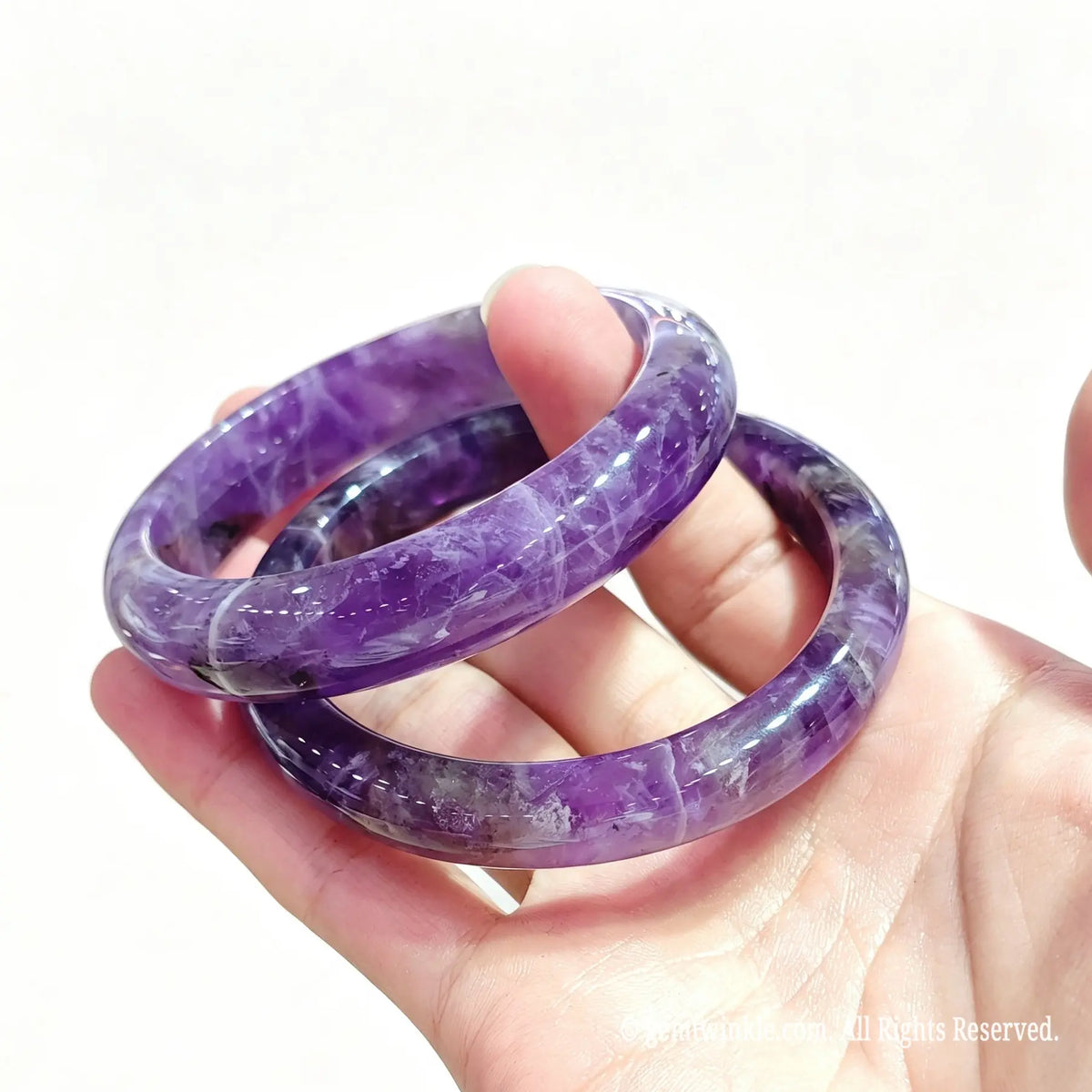 Hand displaying a pair of polished natural dream amethyst bangles with rich purple and white contrast