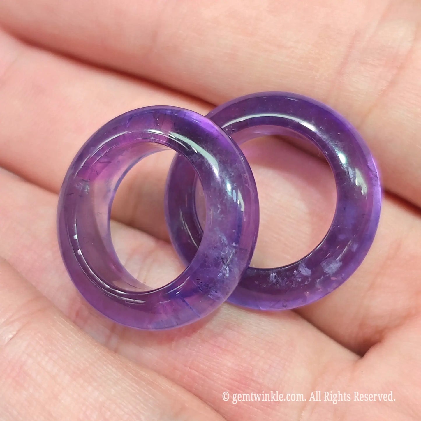 Top view of two natural purple amethyst solid gemstone bands in hand displaying inner diameter roundness