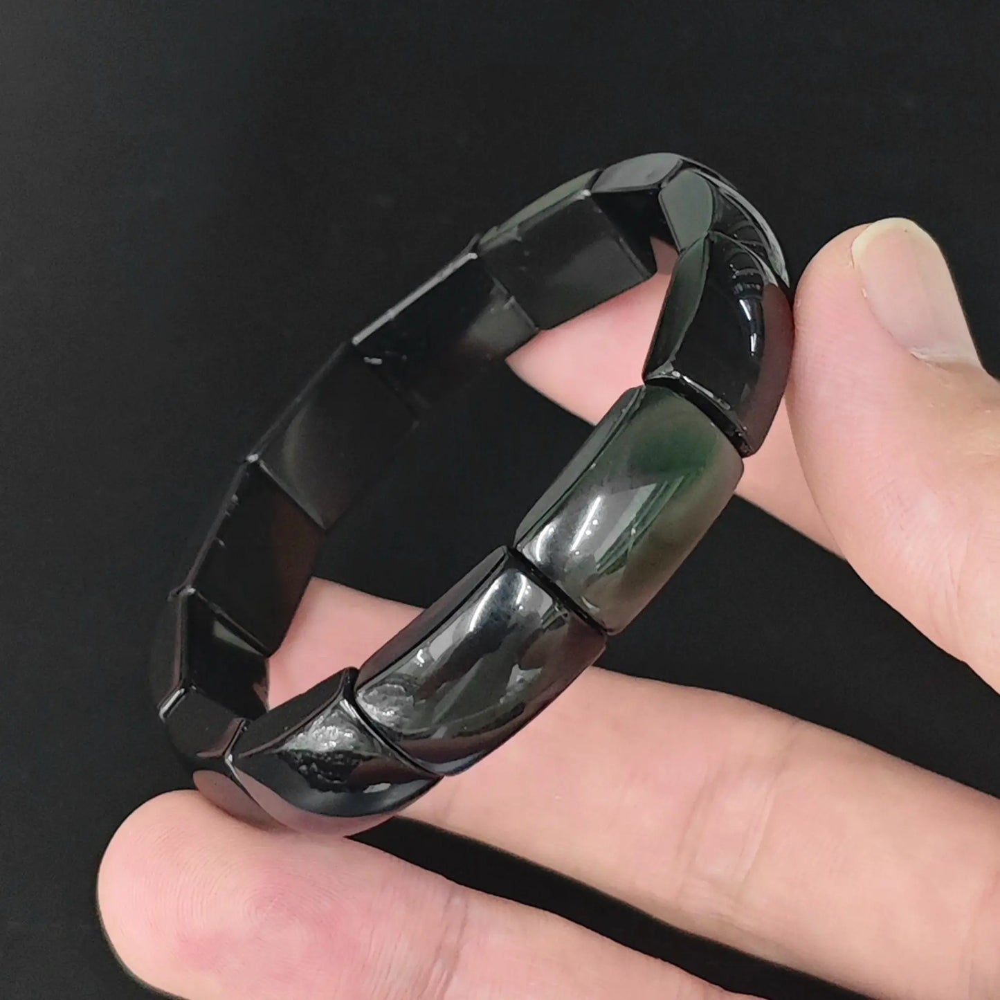 Natural rainbow eye obsidian bangle plate bead bracelet held in hand revealing subtle iridescent sheen on curved plate beads