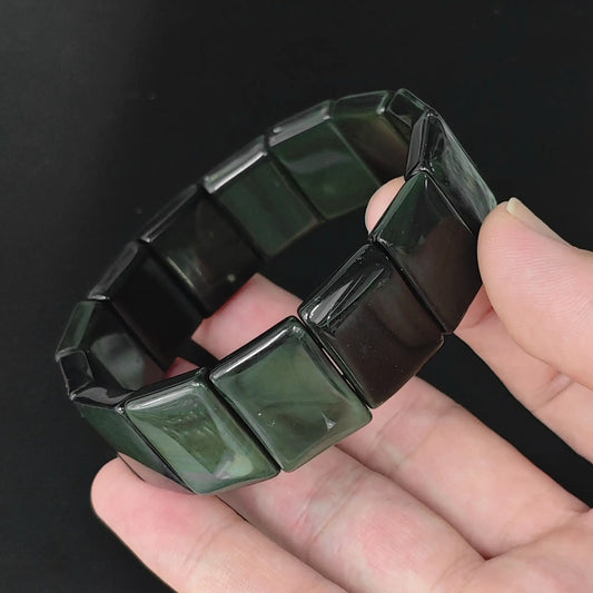 Natural rainbow eye obsidian rectangle plate bead bracelet held in hand revealing subtle iridescent green rainbow sheen