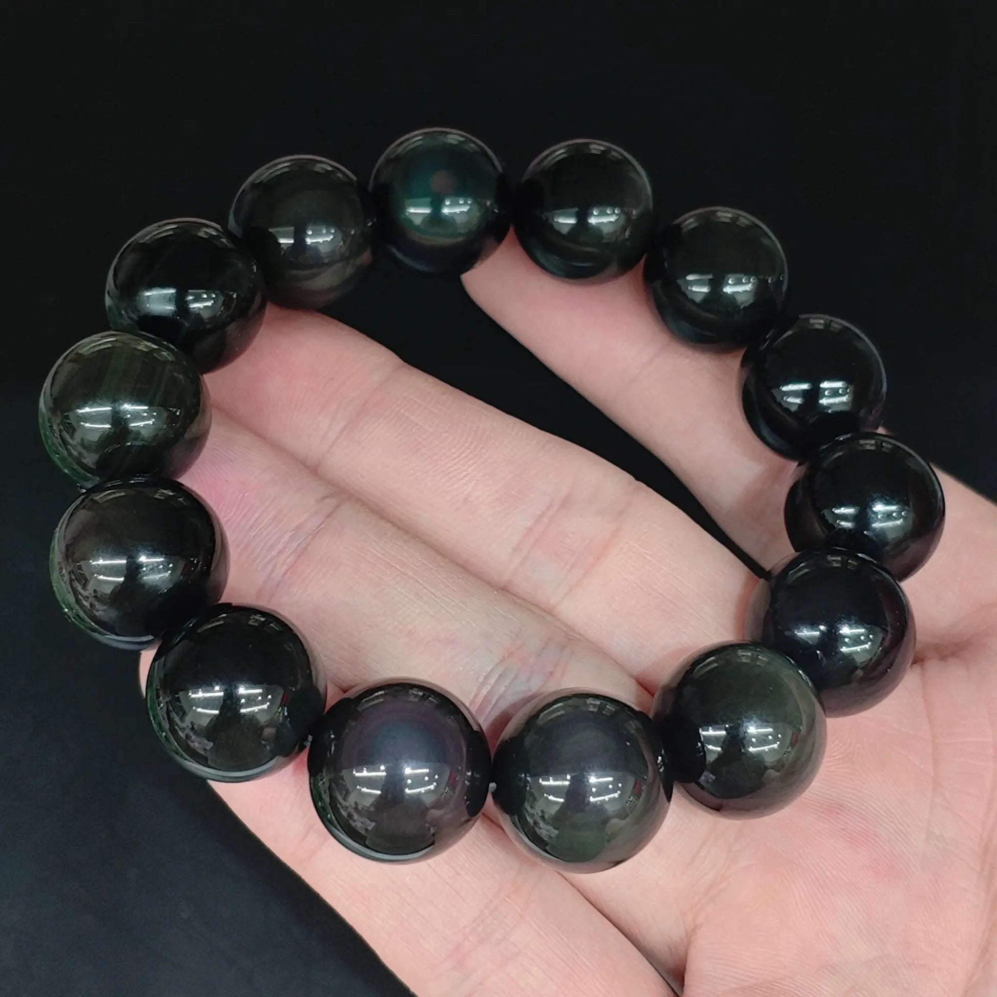 Natural rainbow eye obsidian smooth round bead bracelet held close up showing glossy black finish and rainbow eye sheen