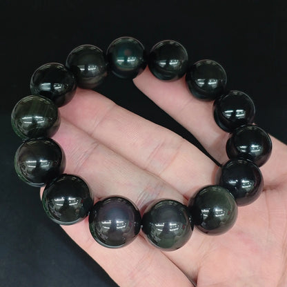 Natural rainbow eye obsidian smooth round bead bracelet held close up showing glossy black finish and rainbow eye sheen