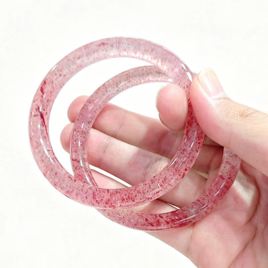 Hand holding two natural quartzite bangles with red mineral inclusions similar to strawberry quartz