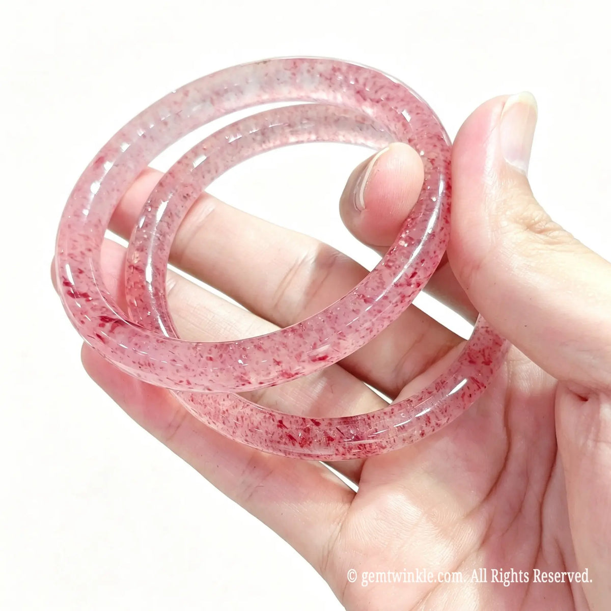 Hand displaying a pair of polished natural red inclusion quartz rock bangles with vibrant red spots