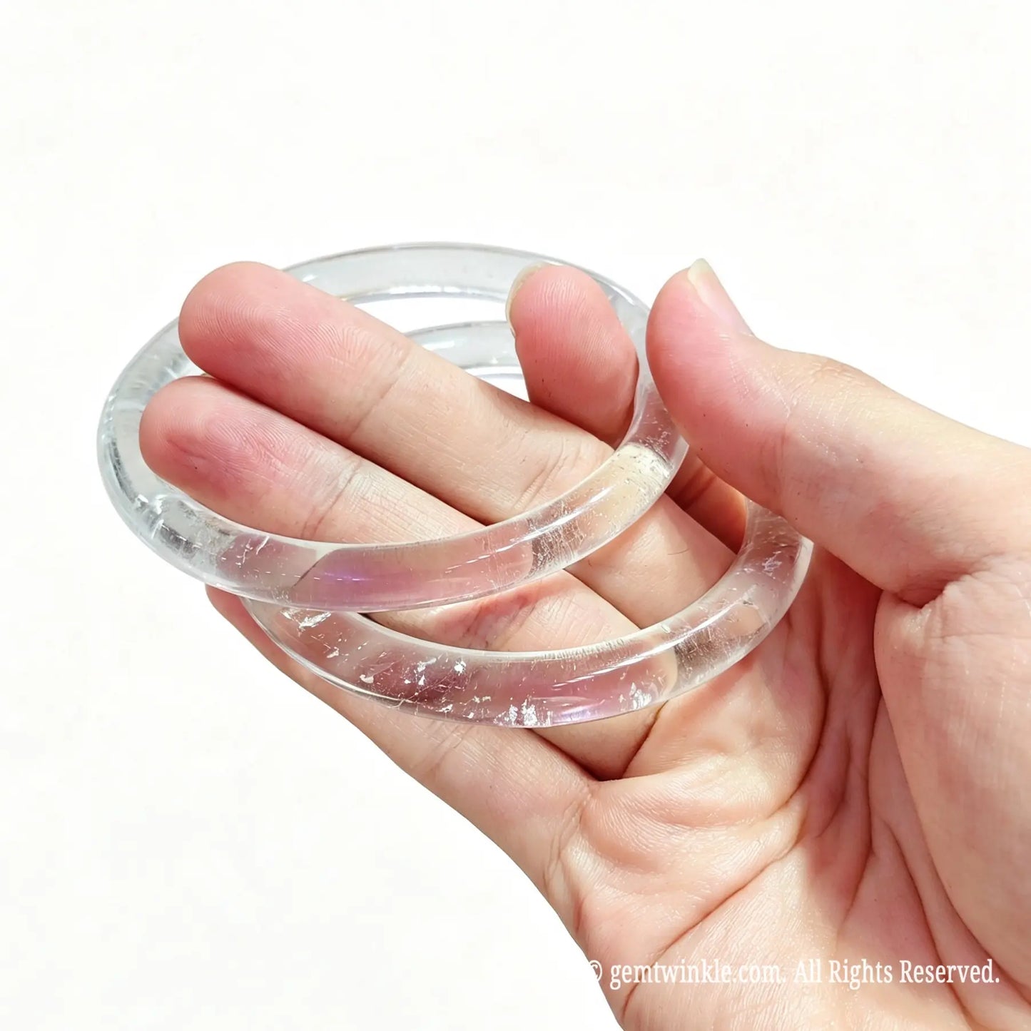 Pair of translucent clear quartz slender bangles held in hand showing smooth polish and minimalist style