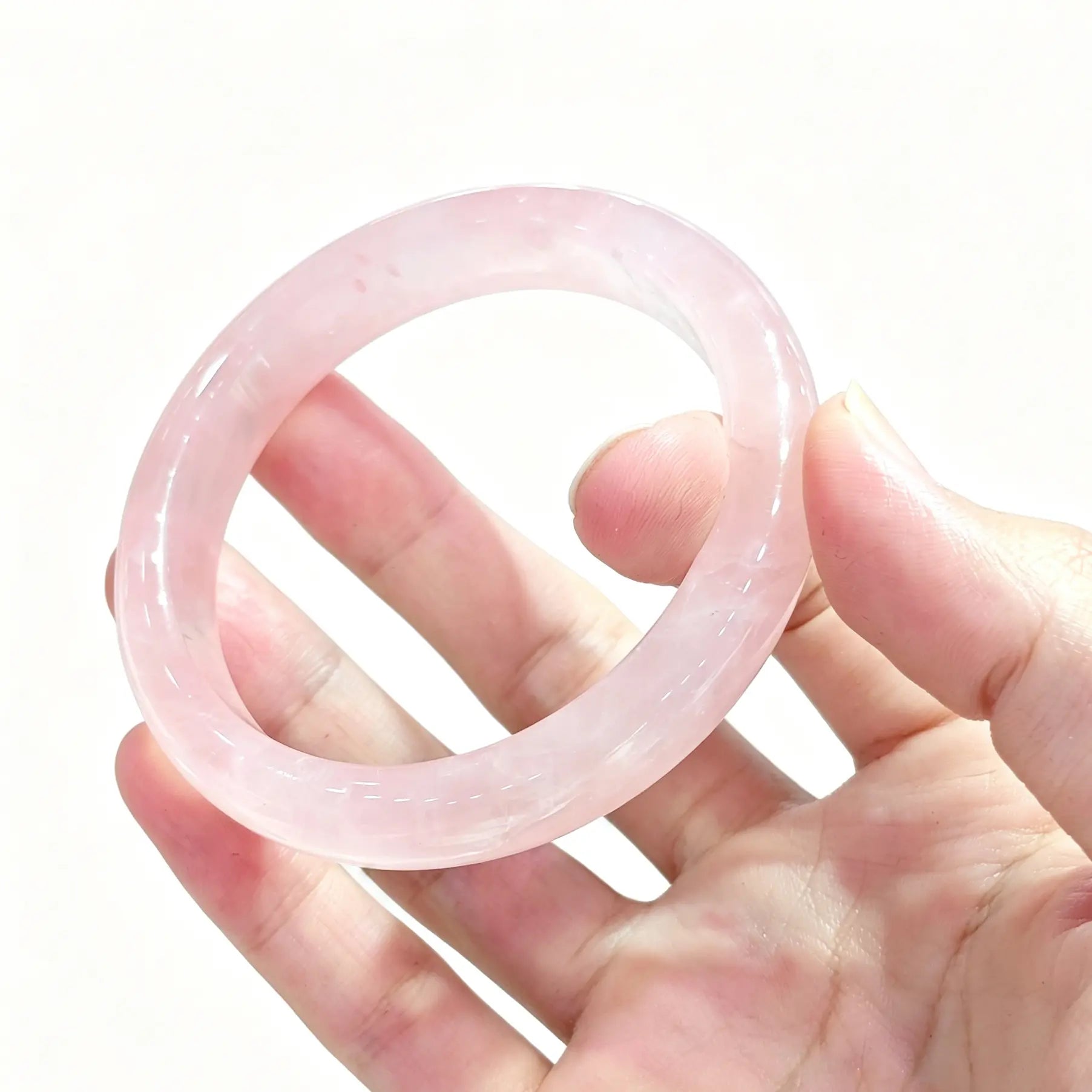 Hand holding a natural rose quartz bangle showcasing soft icy blush pink color and glossy surface finish