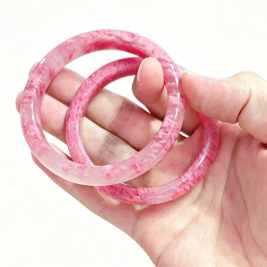 Hand holding a pair of natural rose rhodonite bangles showcasing deep rosy pink tones and smooth polish