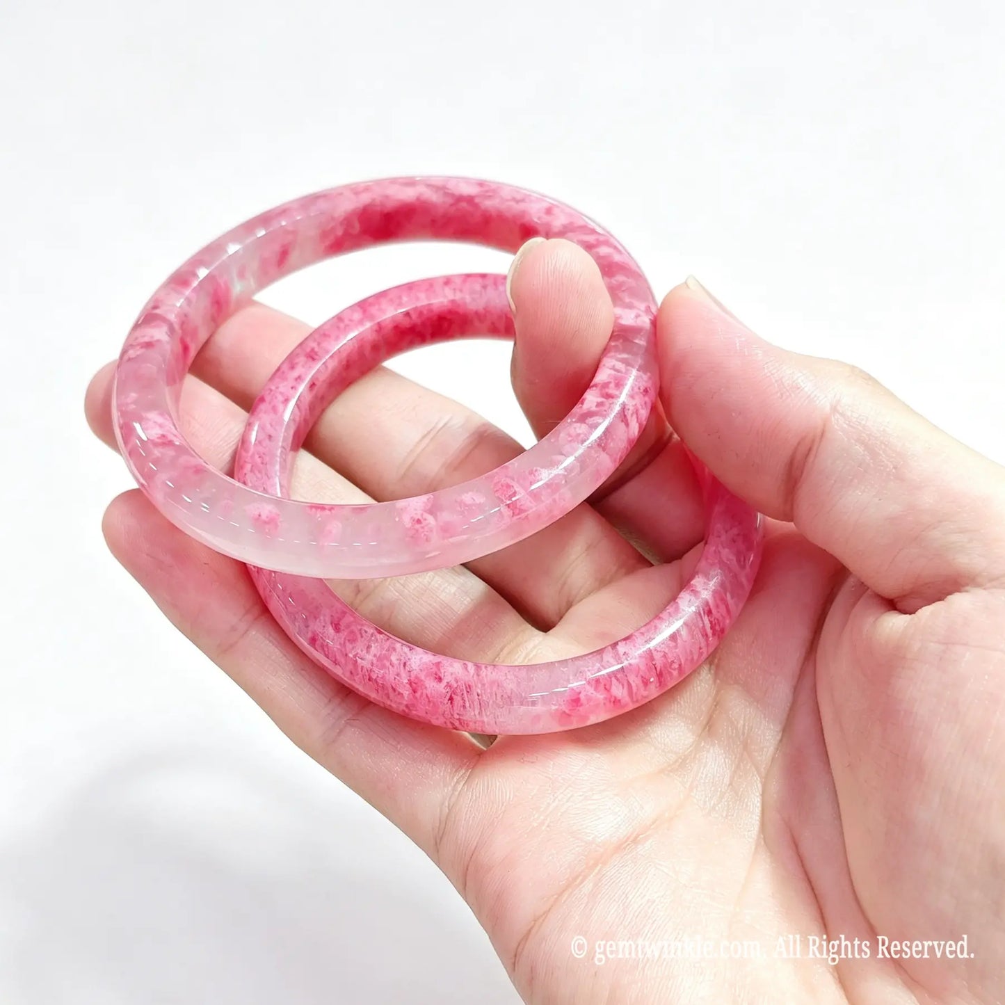 Hand displaying a pair of polished natural rose rhodonite bangles for small shop inventory