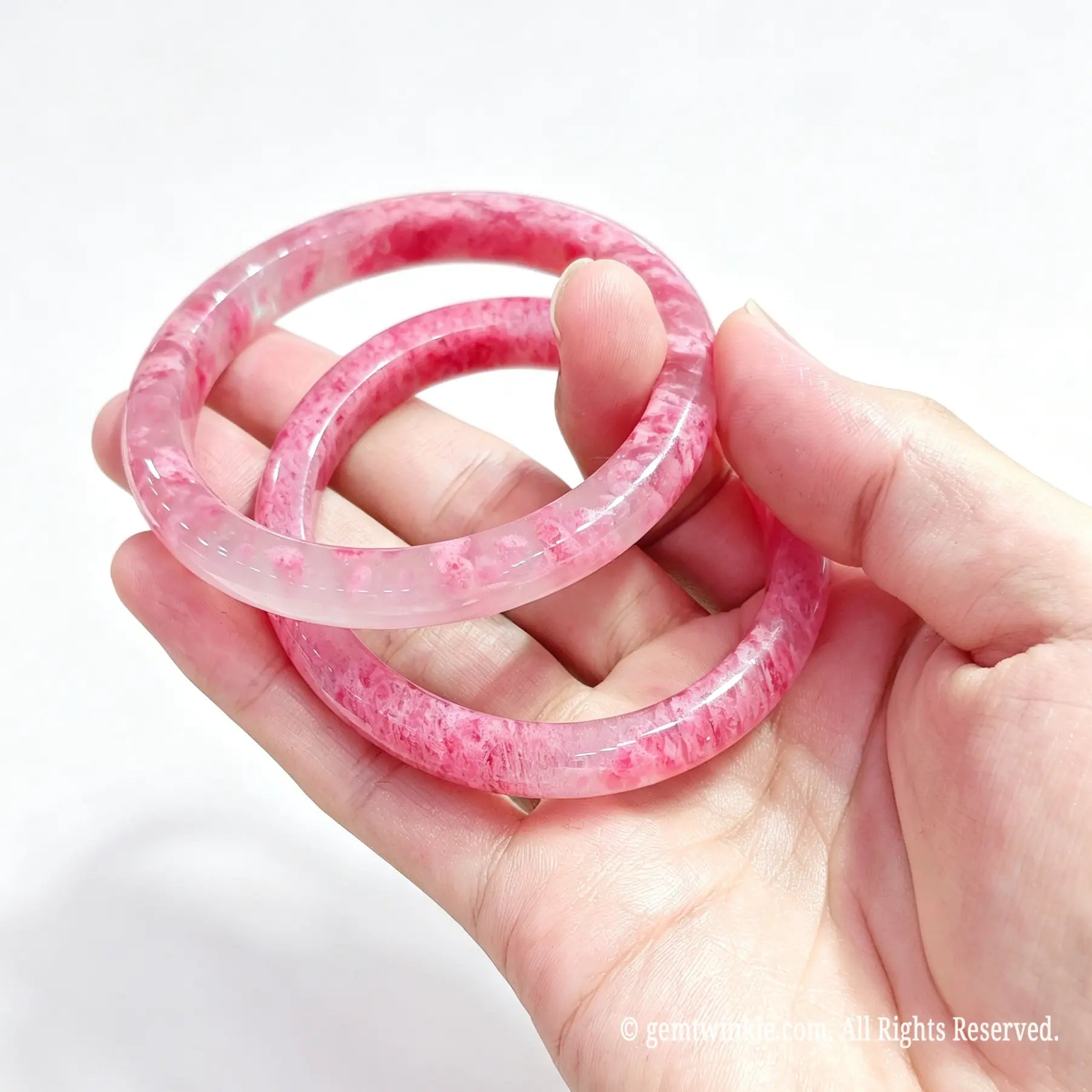 Hand displaying a pair of polished natural rose rhodonite bangles for small shop inventory