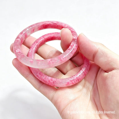 Hand displaying a pair of polished natural rose rhodonite bangles for small shop inventory