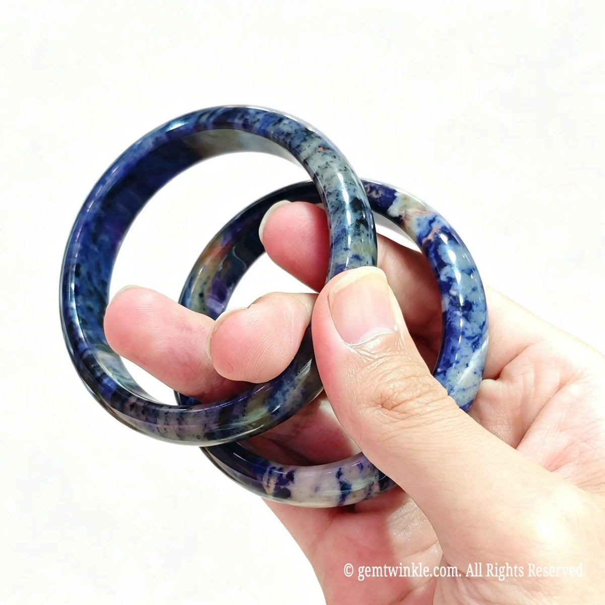 Top view of two natural sodalite bangles held together displaying deep blue tone and calcite patterns