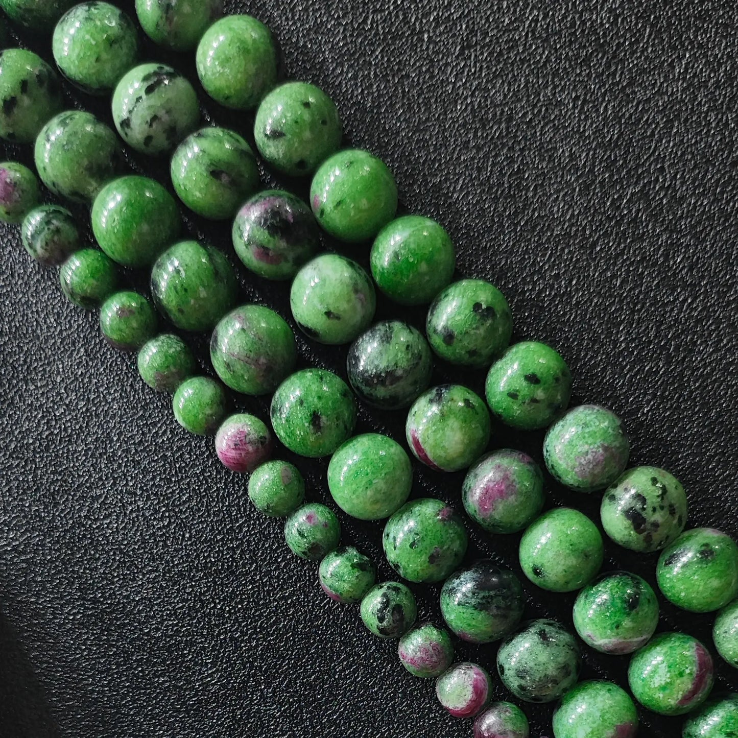 natural ruby in zoisite loose bead strands from six millimeter to twelve millimeter sizes arranged on black background