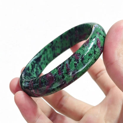 Fingers holding a smooth solid natural ruby in zoisite bangle displaying vivid green zoisite and crimson ruby matrix