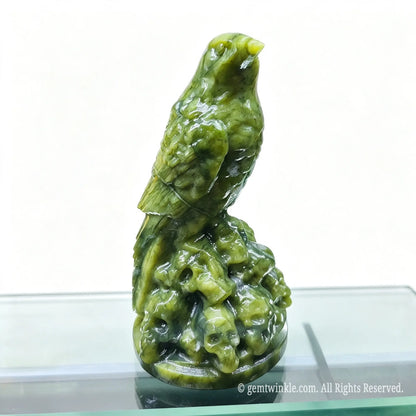 Natural serpentine raven statue 10cm perched on a pile of carved skulls displayed on a glass shelf