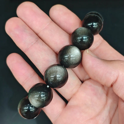 Natural silver obsidian cat's eye beads line held under spotlight displaying concentrated silver sheen and clean matrix