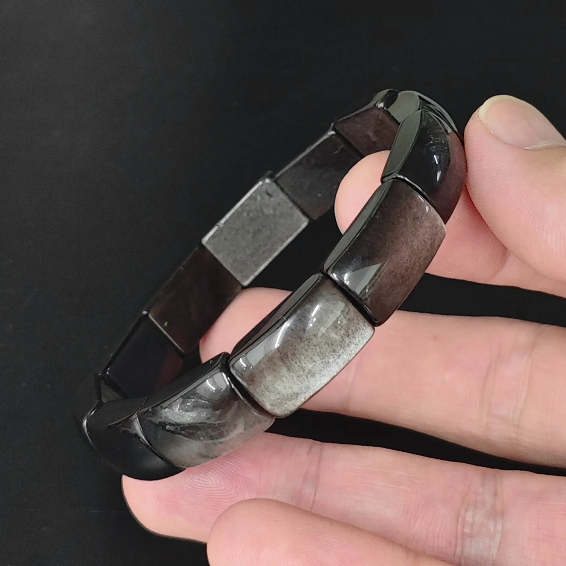Natural silver sheen obsidian 16mm rectangle plate bead bracelet held in hand revealing bright silvery schiller flash