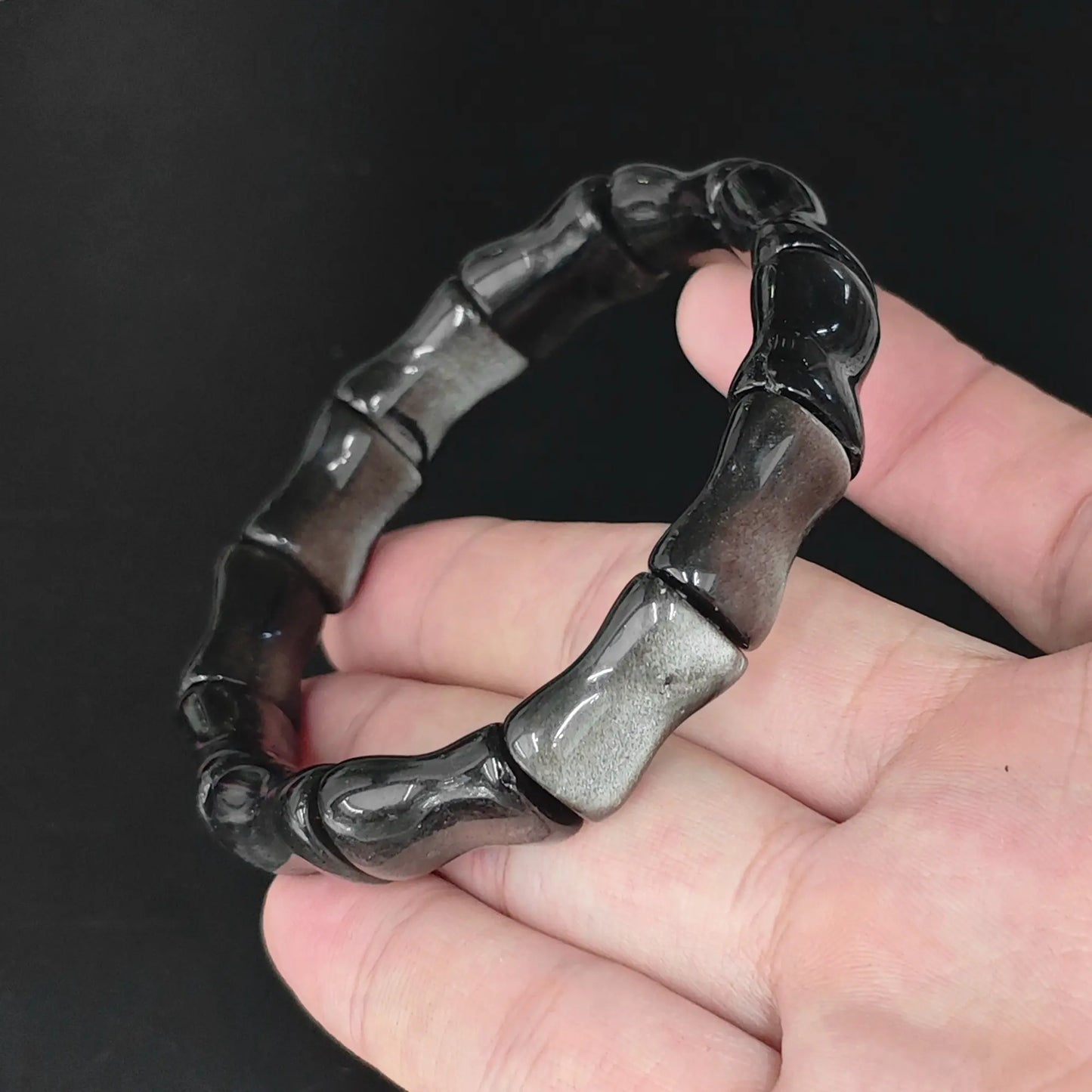 Natural silver sheen obsidian bamboo joint bead bracelet held in hand revealing bright silvery schiller flash
