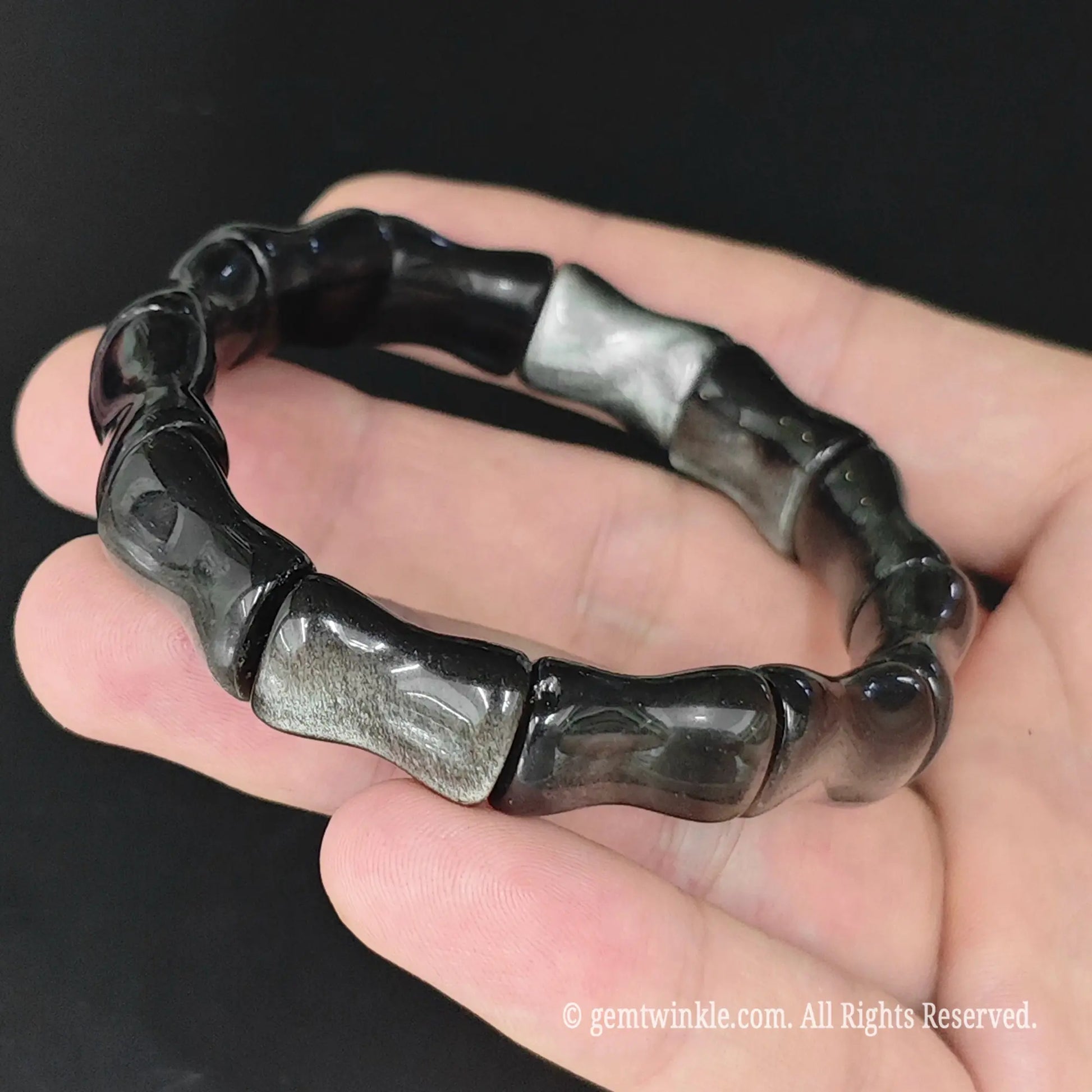 Natural silver sheen obsidian bamboo joint cuff bracelet held in open palm displaying metallic silver sheen reflection