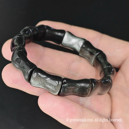 Natural silver sheen obsidian bamboo joint cuff bracelet held in open palm displaying metallic silver sheen reflection