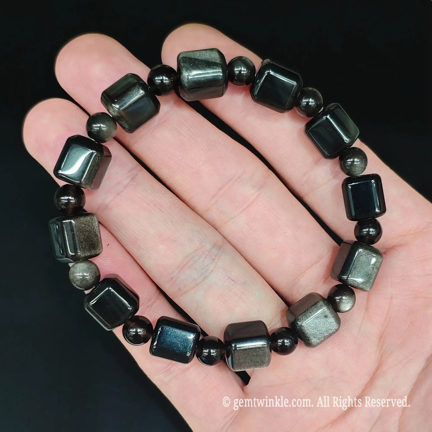 Natural silver sheen obsidian cube stretch bracelet held under spotlight showing reflective silver eye optical halos