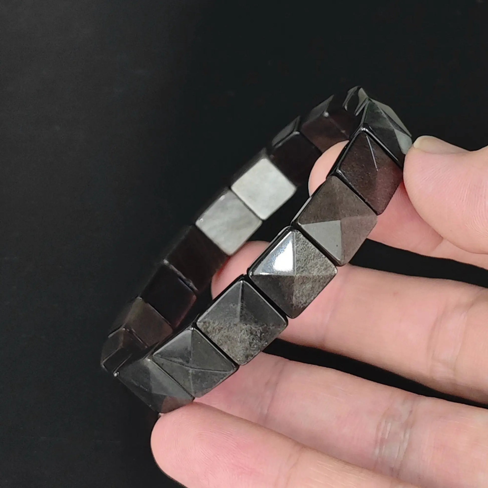 Natural silver sheen obsidian pyramid cut 11mm square bead bracelet held in hand showing bright metallic flash across faceted surfaces