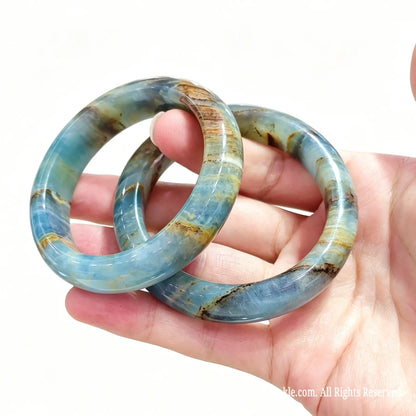 Pair of natural blue calcite bangles held in hand showing smooth polish and earth-toned aragonite veins