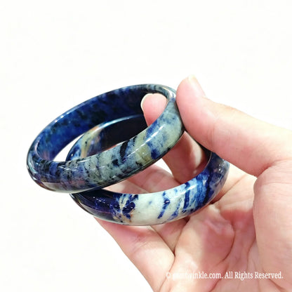 Hand displaying a pair of polished natural blue sodalite bangles for boutique inventory