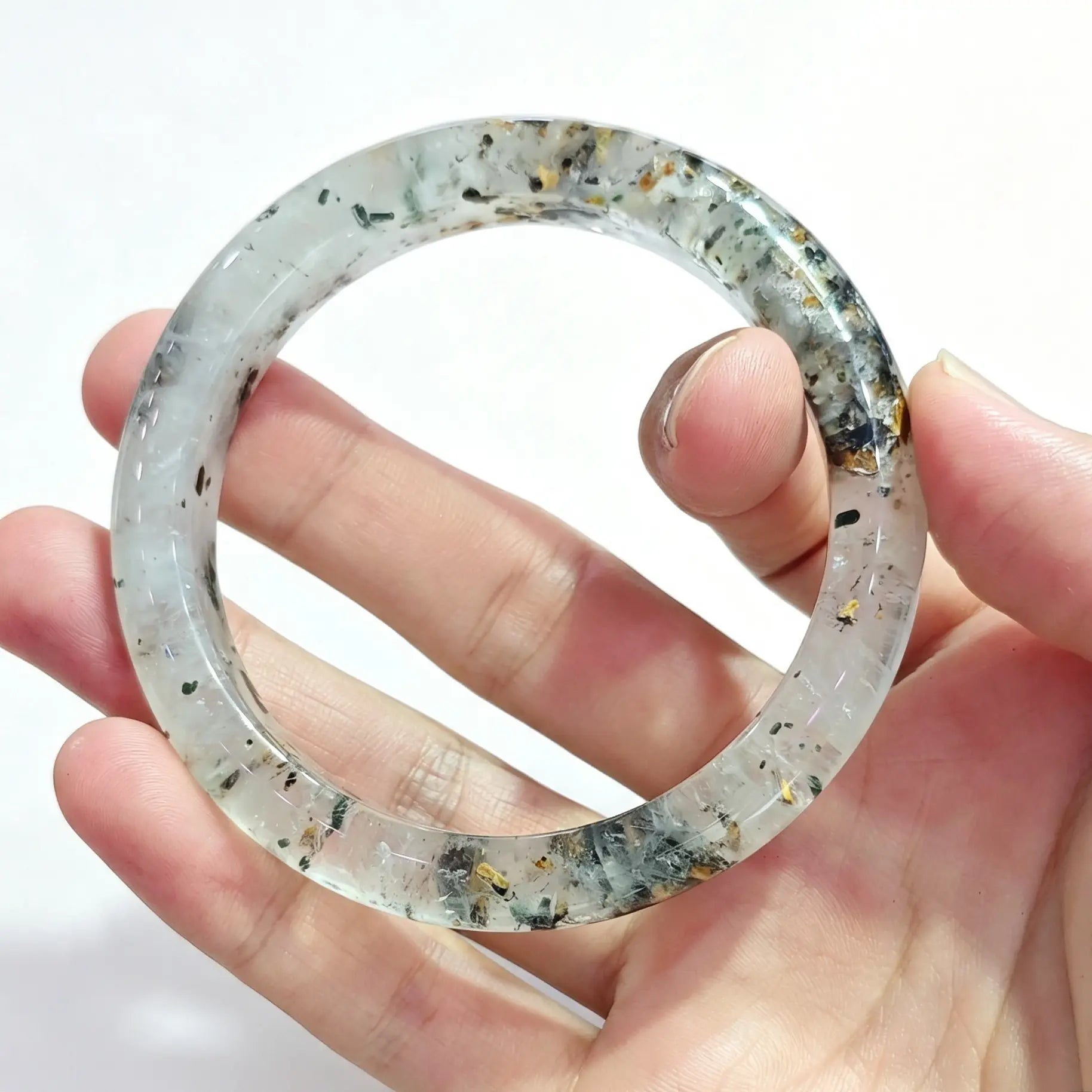 Fingers holding a smooth solid three lives stone quartz bangle displaying translucent crystal with multi mineral speckles
