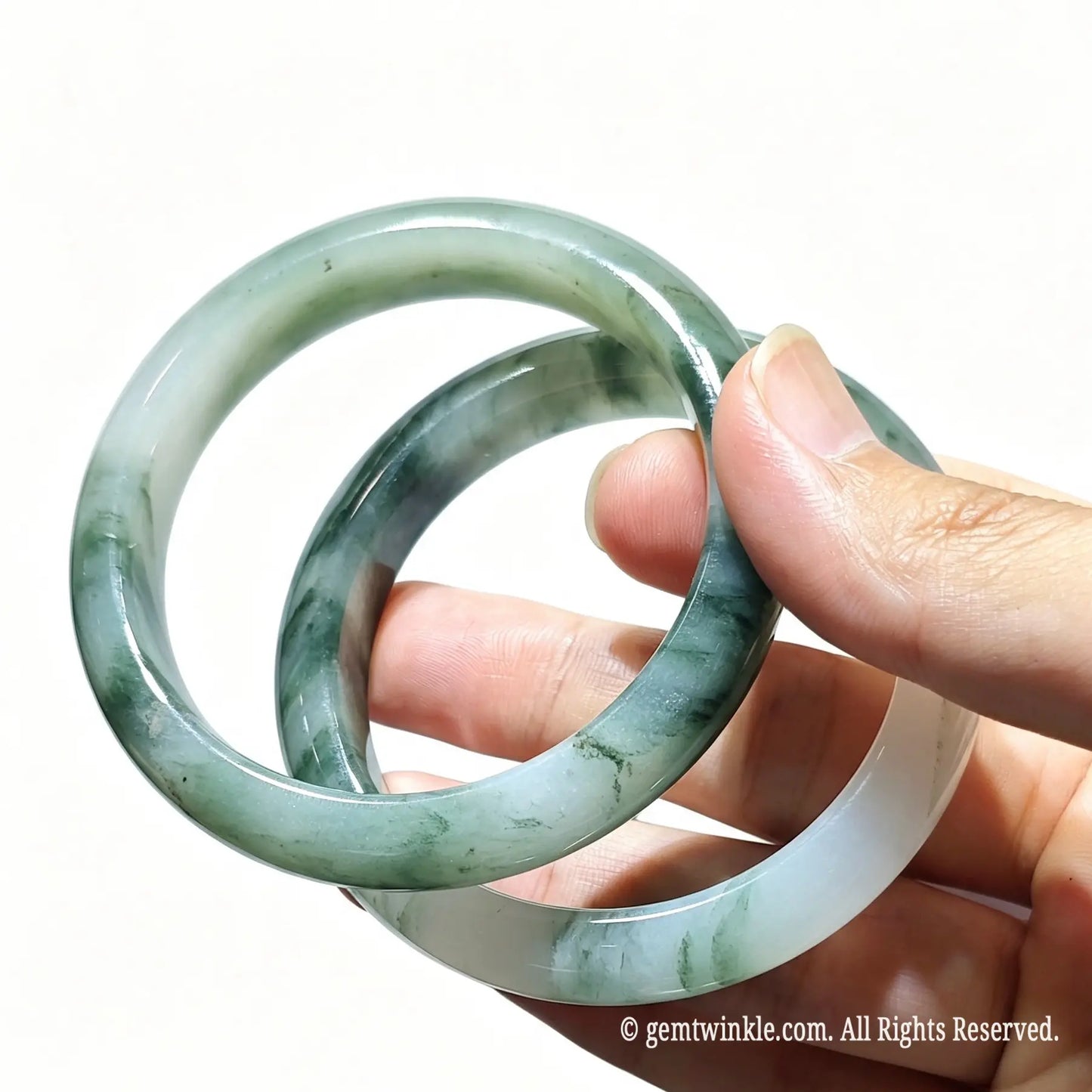 Pair of natural tianshan green quartzite jade bangles held in hand displaying translucent icy texture