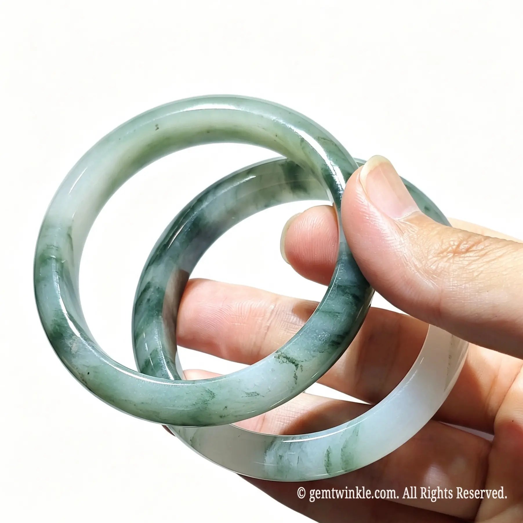 Pair of natural tianshan green quartzite jade bangles held in hand displaying translucent icy texture