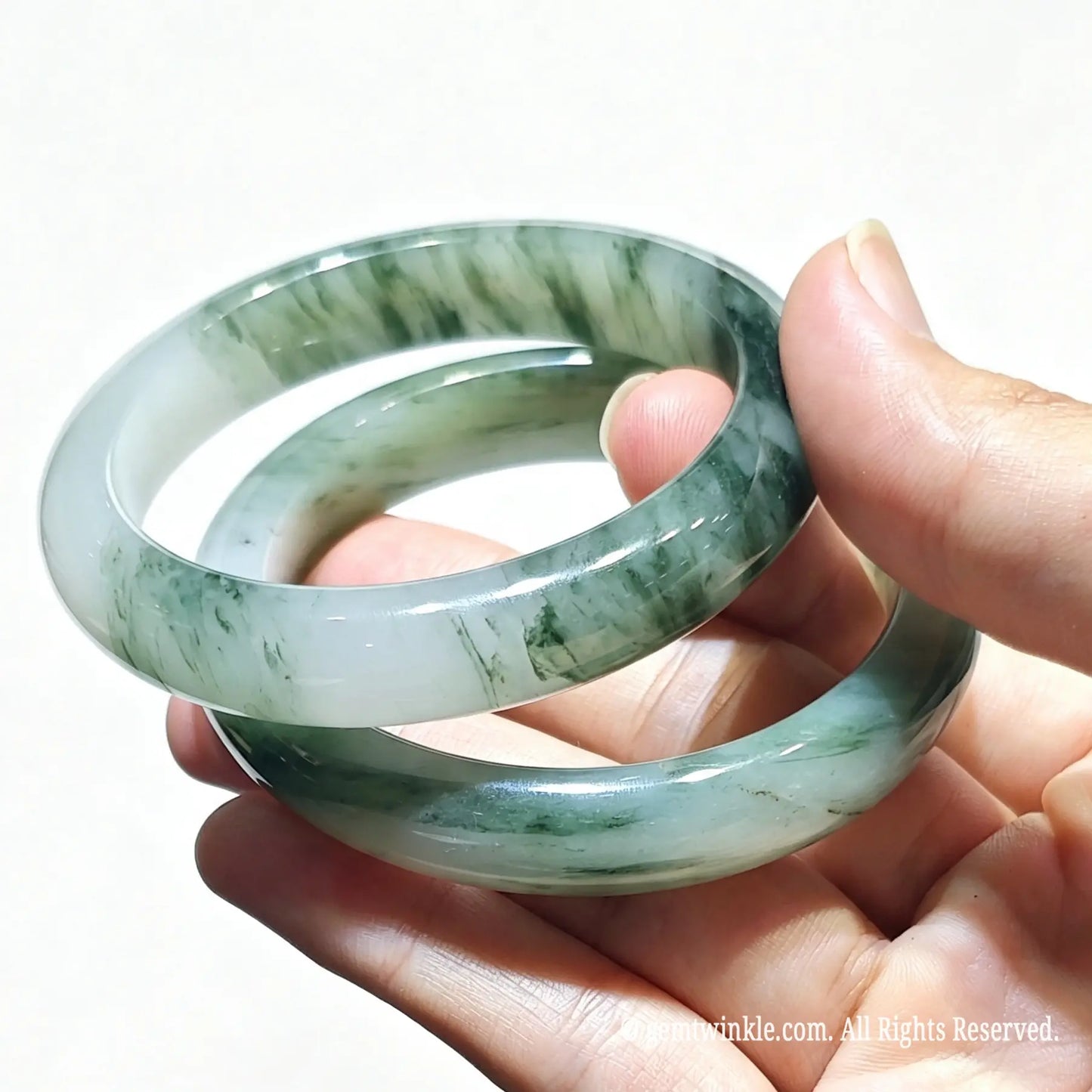 Hand holding a pair of natural tianshan green quartzite bangles with icy base and green floating silk threads