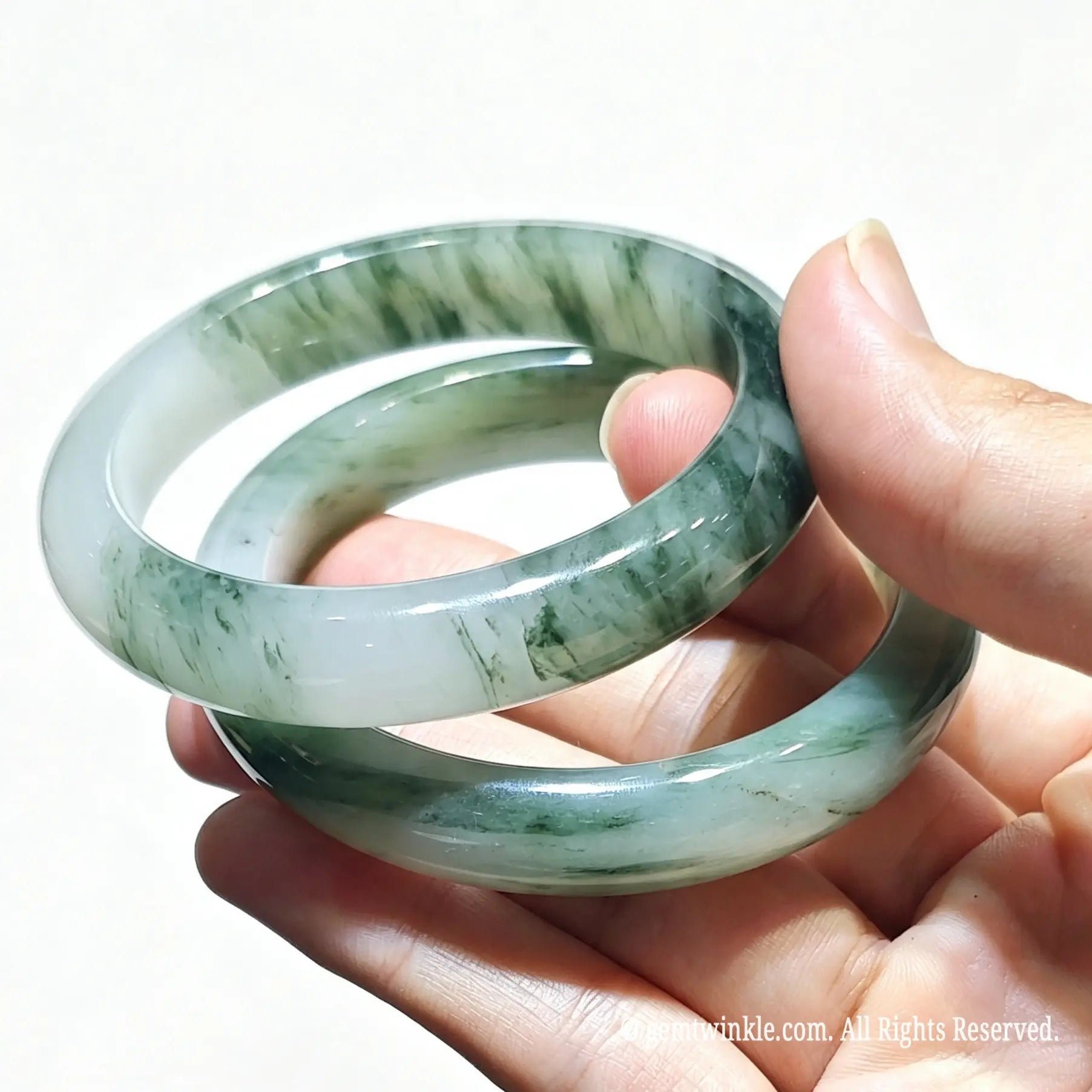 Hand holding a pair of natural tianshan green quartzite bangles with icy base and green floating silk threads