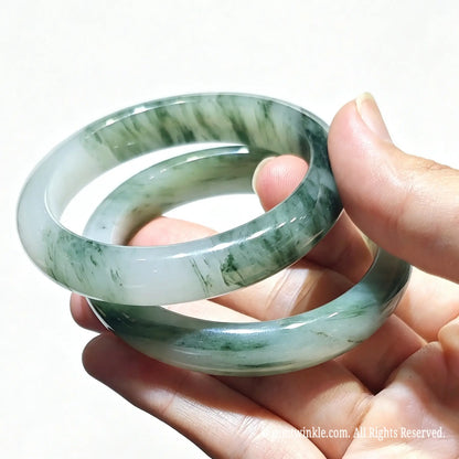 Hand holding a pair of natural tianshan green quartzite bangles with icy base and green floating silk threads