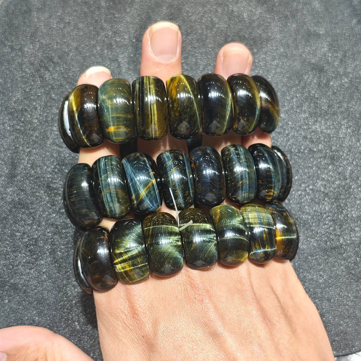 three natural tiger eye barrel bead stretch bracelets lined up neatly across hand displaying golden and blue silk bands