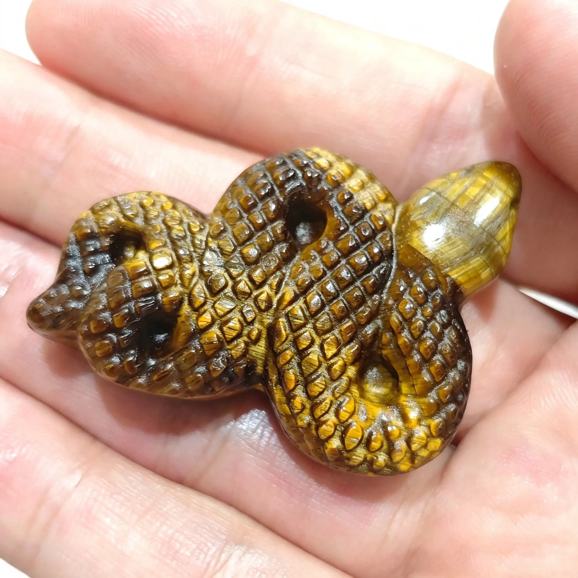 Natural yellow tiger eye snake carving 5cm held in hand showing detailed carved scales and golden chatoyancy