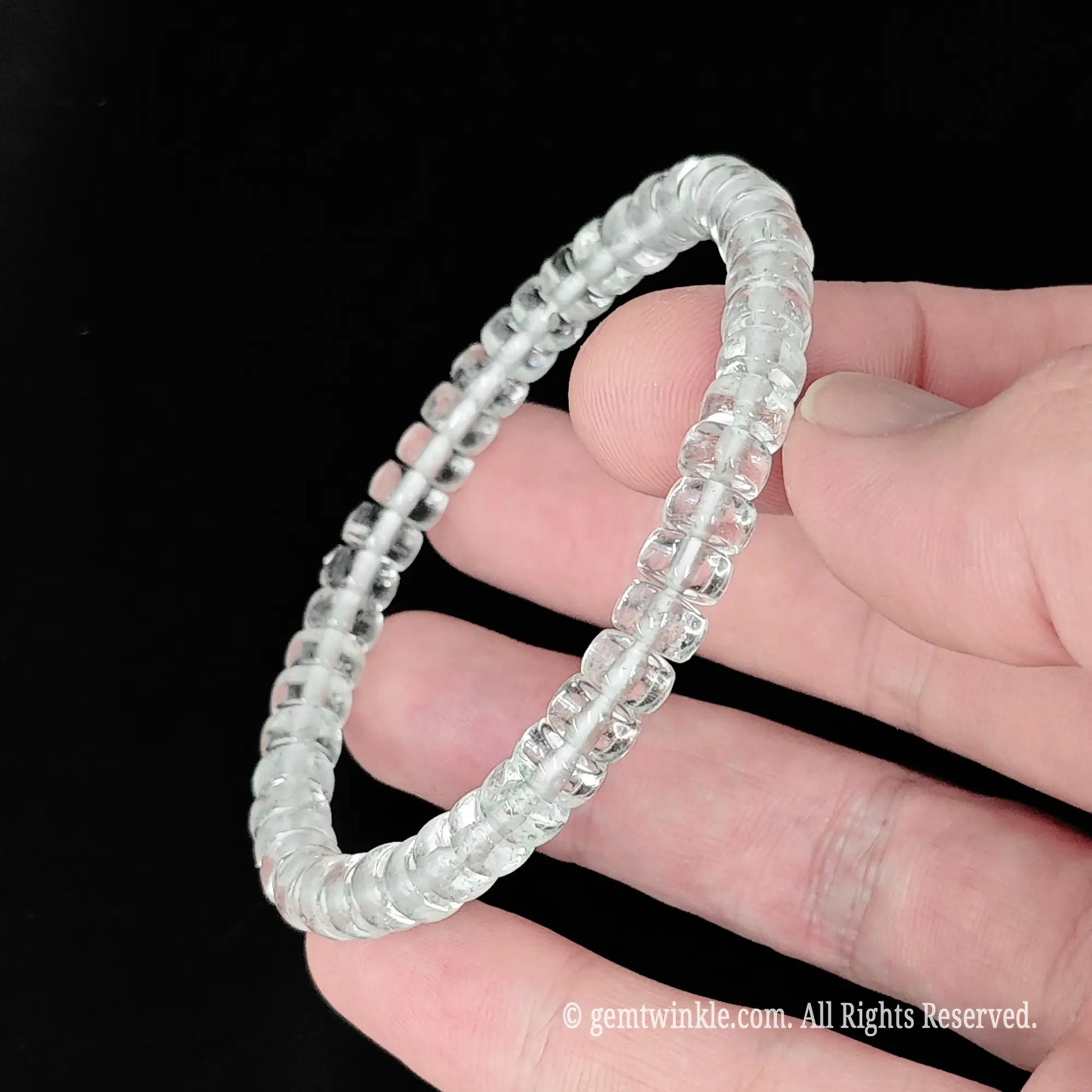 Natural white crystal small wheel bead bracelet held across fingers showing smooth disc alignment and glossy finish