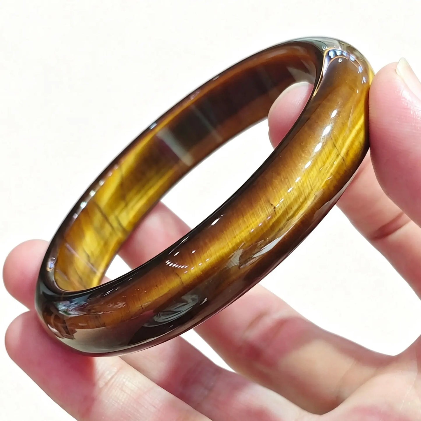 Fingers holding a smooth solid yellow tiger eye bangle displaying rich golden amber chatoyancy and silky luster