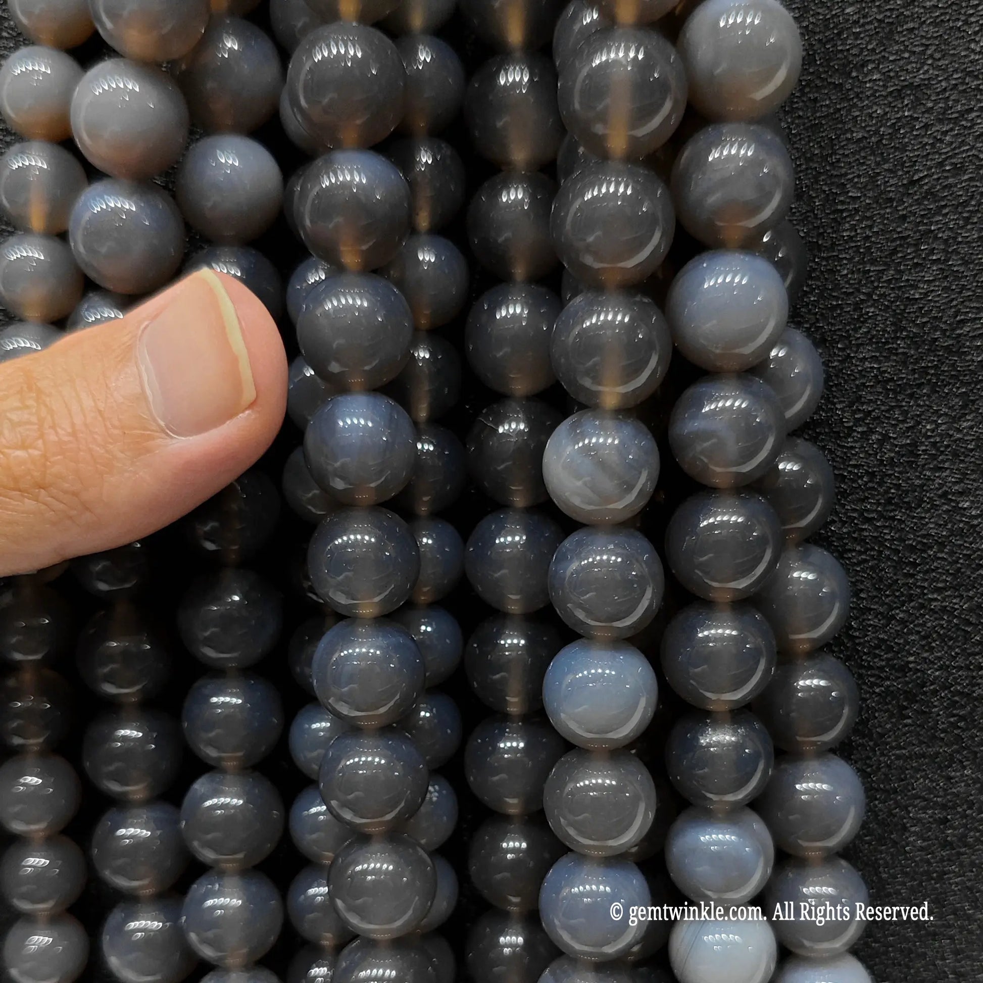 Inspecting a bundle of diverse sizes of neutral grey agate round beads from 4mm to 14mm with finger for scale reference