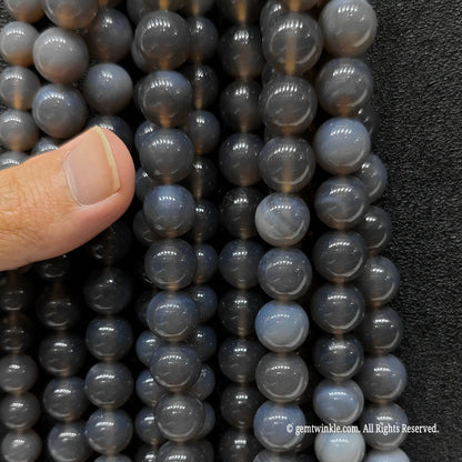 Inspecting a bundle of diverse sizes of neutral grey agate round beads from 4mm to 14mm with finger for scale reference