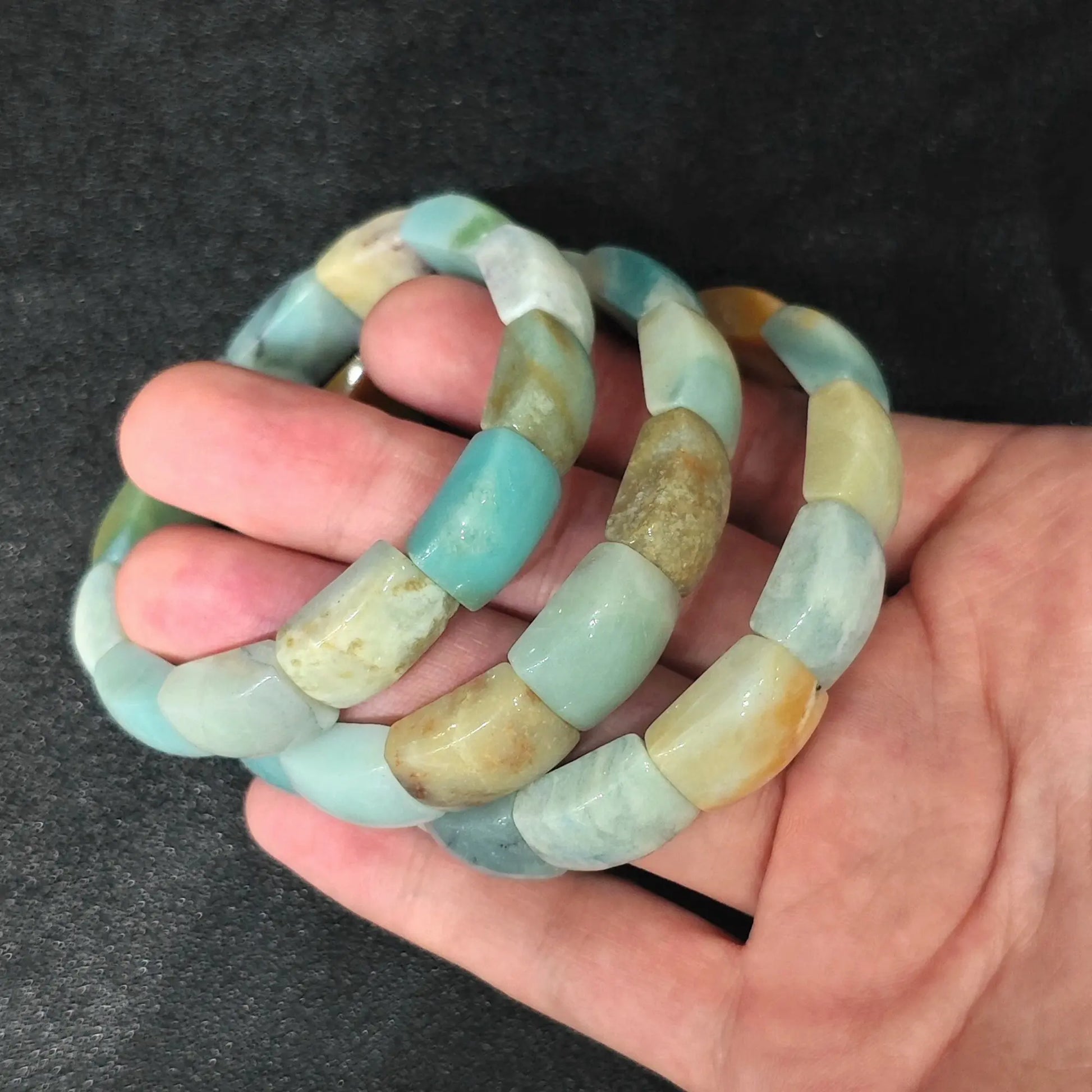 Palm view of Caribbean Calcite flat profile barrel bead stretch bracelets showcasing sea blue and tan color contrast