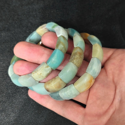 Palm view of Caribbean Calcite flat profile barrel bead stretch bracelets showcasing sea blue and tan color contrast