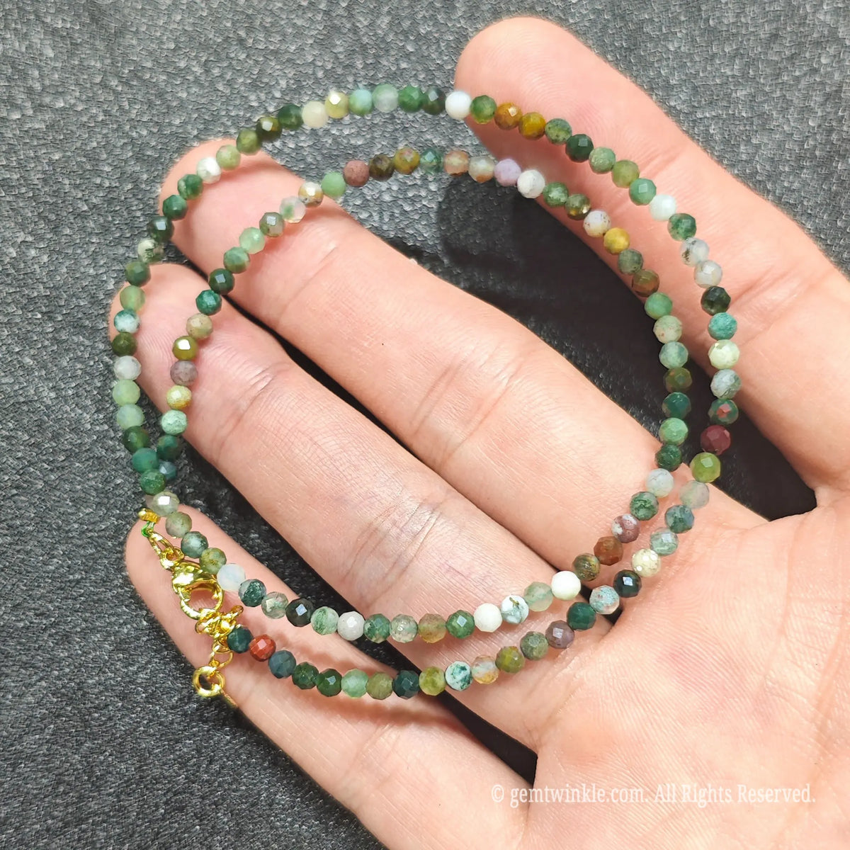 Hand holding 3mm faceted ocean jasper necklace revealing multicolored orbicular chalcedony patterns