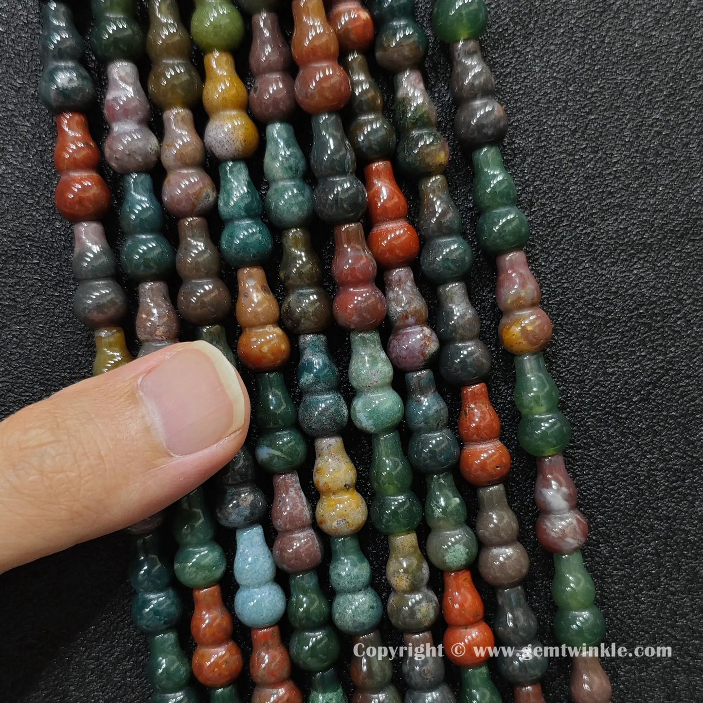 Close up view of natural ocean jasper calabash beads held on fingers for quality preview