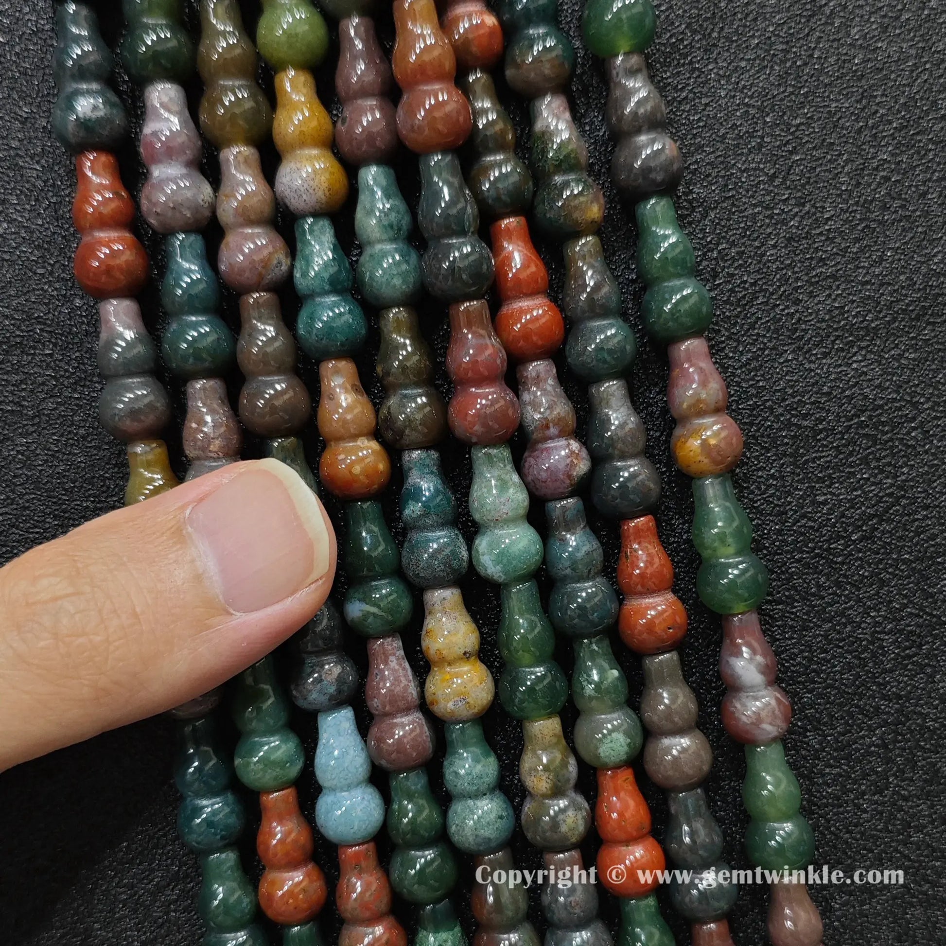 Close up view of natural ocean jasper calabash beads held on fingers for quality preview