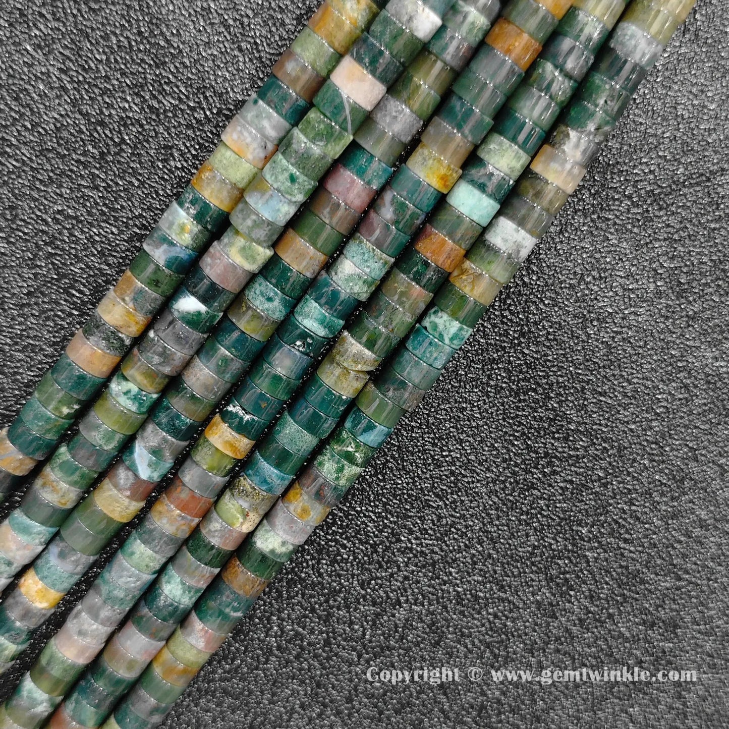Angled view of natural ocean jasper flat disc gemstone strands arranged parallel on dark background